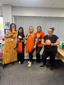 Group of five staff members in an office setting wearing orange clothing and accessories posing at the camera.