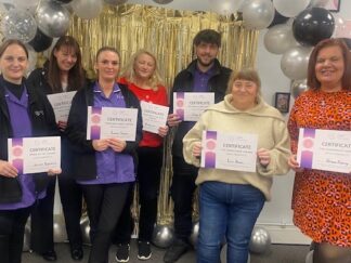 Group of CRT care workers in uniform with gold decorations and balloons in the background.